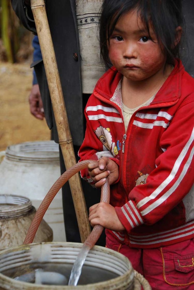 木汪村小女孩将水引到自家的水桶里
