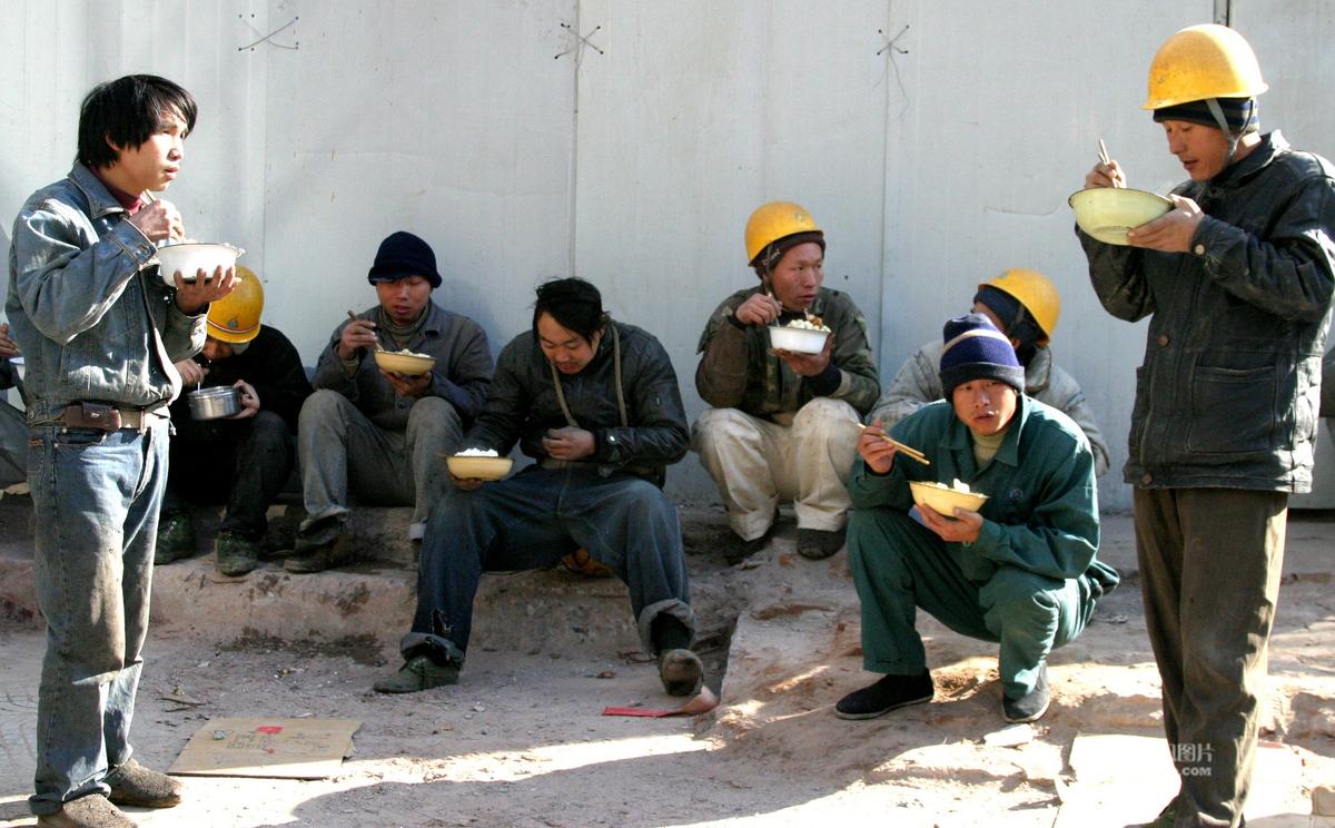 劳动者的午餐:2006年11月30日,8个民工在墙边有蹲有站的吃午饭.