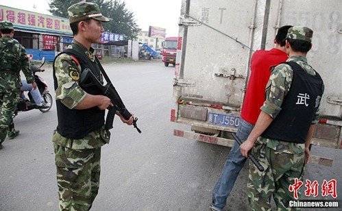 图为持冲锋枪的武警要求检查一辆货车的后箱.