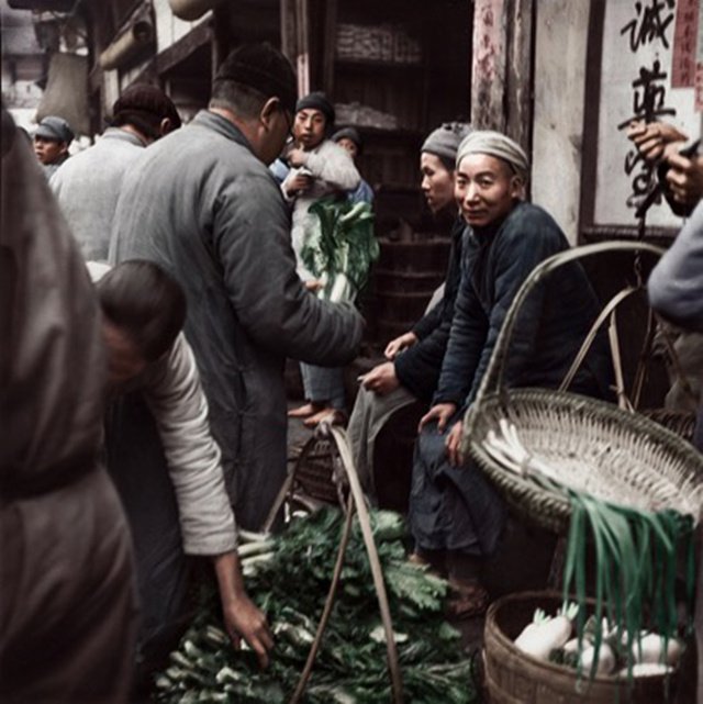 一位卖菜的农民正看着摄影师微笑，他面前竹筐里成捆的青菜是川渝地区制作酸菜和盐菜的主要材料。（上色版）