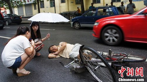 老者骑车突发病倒地 俩女大学生车流中撑伞守护