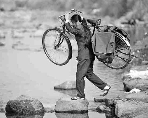 在送邮件的路上,罗细英扛着自行车过河.美联社
