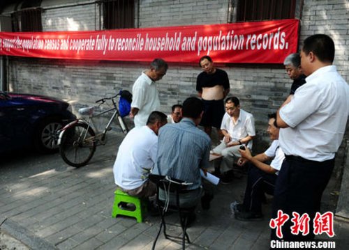 资料图：2010年9月6日下午，北京国子监胡同，市民们在路边下棋休闲，身后的墙上挂着用英语书写的“支持人口普查”内容的条幅。中新社记者 侯宇 摄