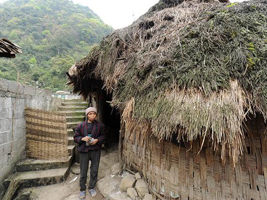 贵州省荔波县瑶山乡巴平村弄哄组，66岁的村民蒙二妹站在自家居住的房屋前，她和儿子兰金华住的茅草房已有几十年历史，是用树枝、竹片拼成的（3月22日摄）。 新华社记者 陶亮 摄