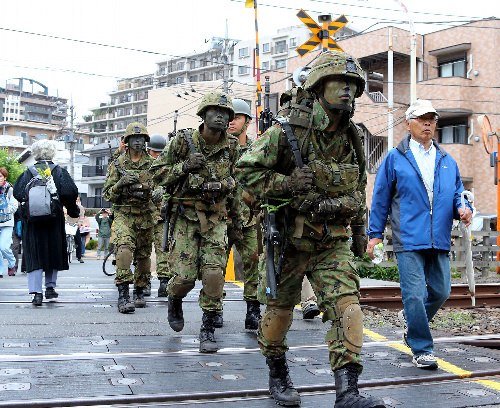 日本陆上自卫队队员12日身穿迷彩服,手持武器出现在东京街头