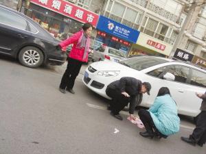 一位过路司机帮助捡钱,一位红衣女士现场示意行人不要靠近.