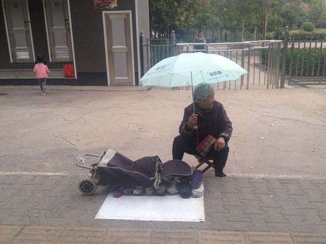 看哭！郑州七旬老太为贴补家用 雨中撑伞卖鞋垫