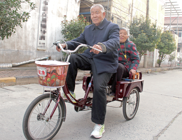 在沁园路与东夫大街交织口,一位老人骑三轮车载着另一位老人往马路另