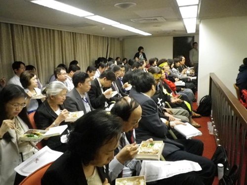 台湾“劳委会”官员备询时，坐在绝食工人(头绑黄布条)旁吃便当。(图／台湾东森电视台网站)