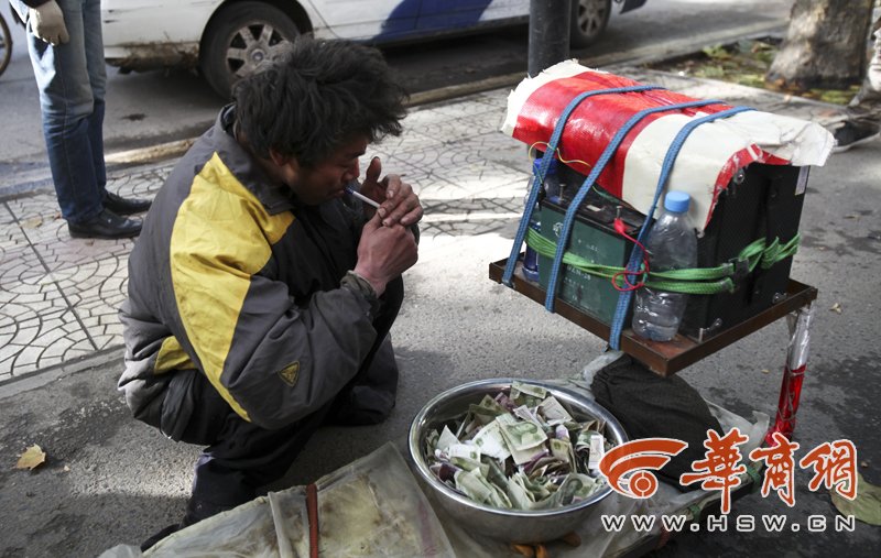 "残疾"乞丐蹲在自己的道具旁抽烟. 本报记者 黄利健 摄