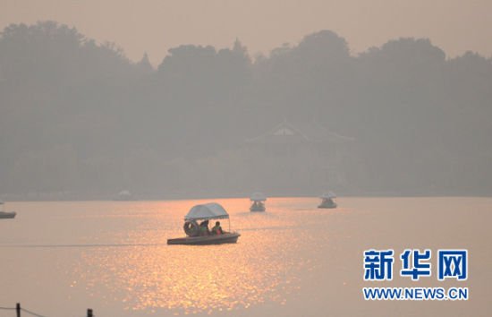  12月4日，几条游船在夕阳的映射下，划过雾霾笼罩中的杭州西湖。据杭州市环保局通报，12月4日中午，杭州市环境空气质量24小时AQI指数达到278，首要污染物为PM2.5，类别为重度污染。杭州市气象台当日上午发布霾黄色预警信号，中午升级为霾橙色预警信号。新华社记者 王定昶摄