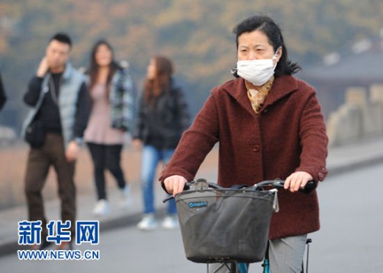  12月4日，一位行人戴着口罩骑行在杭州西湖白堤上。据杭州市环保局通报，12月4日中午，杭州市环境空气质量24小时AQI指数达到278，首要污染物为PM2.5，类别为重度污染。杭州市气象台当日上午发布霾黄色预警信号，中午升级为霾橙色预警信号。新华社记者王定昶摄 