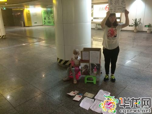 今日下午，重庆两路口轻轨站，陈得娟举着牌子，女儿则坐在她的身边。 实习记者 艾俊锋 摄