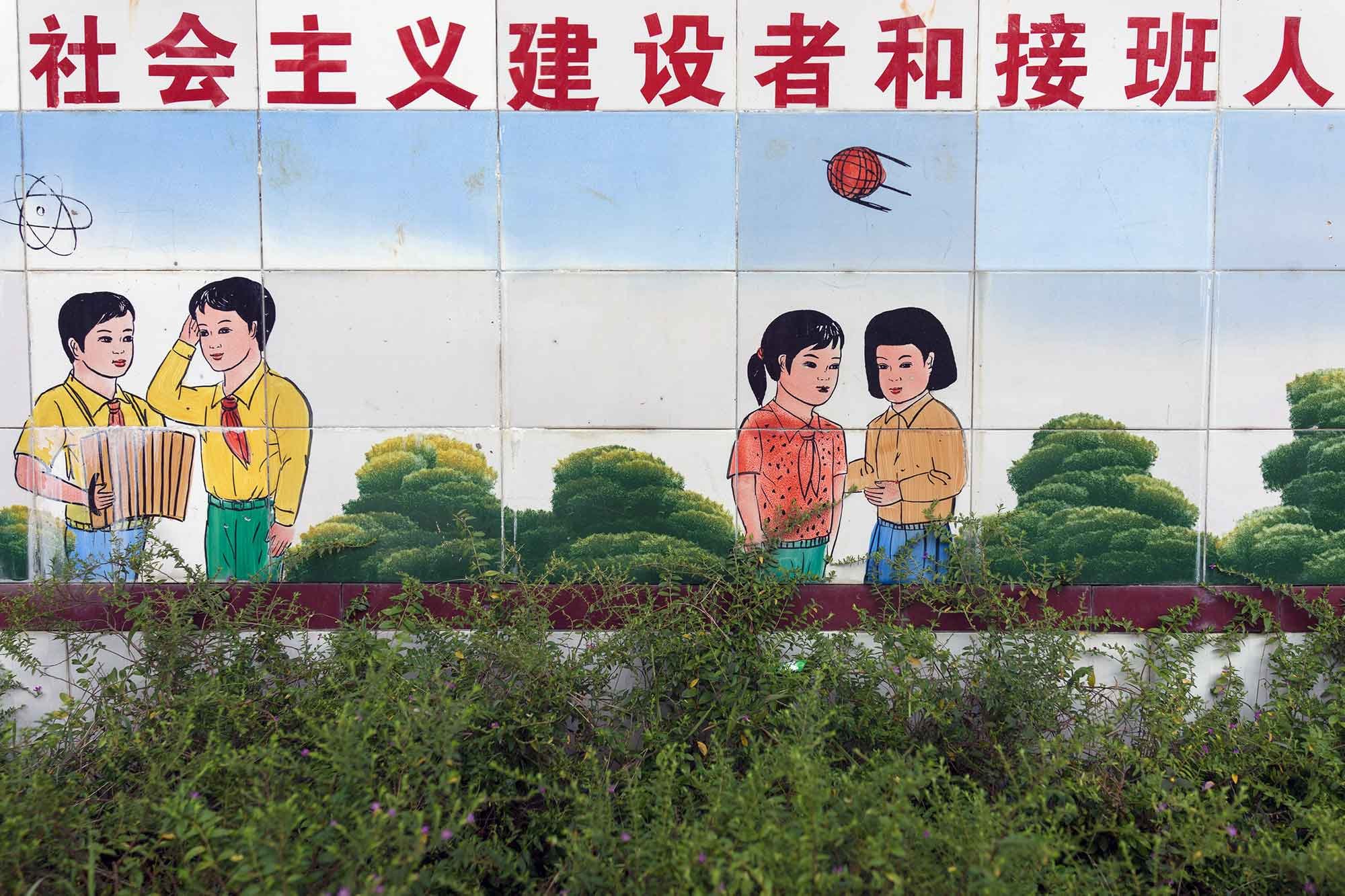 莽人小学生和学校的瓷砖壁画。现在莽人的几个村落中都已经建起了小学校。而在2016年,南科村甚至建起了幼儿园。 莽人小学生和学校的瓷砖壁画。现在莽人的几个村落中都已经建起了小学校。而在2016年,南科村甚至建起了幼儿园。