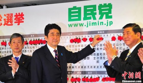 图为12月16日，自民党总裁安倍晋三（中）为当选议员贴获胜标志红花。中新社发 孙冉 摄