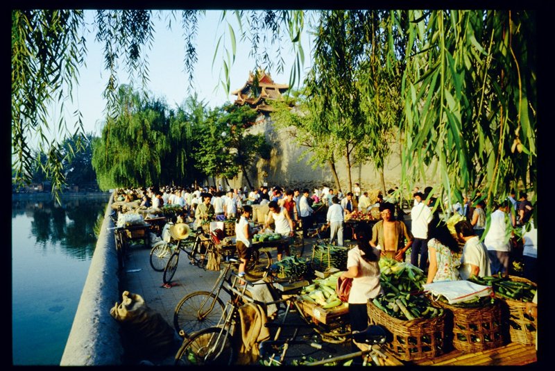 早市是京城百姓生活的一大特色。20世纪80年代初期,早市开始逐渐活跃起来。早市起初是为解决市民购买蔬菜水果方便,以及安置个体就业而设,后来逐渐扩大到售卖各种日用百货。早市一般设在皇城根附近或人口密集的街区,自天蒙蒙亮就开始,一直到中午前闭市。图为清晨,小贩们蹬三轮车载着新鲜的蔬菜到早市出售,早市背靠紫禁城,面对筒子河,老北京的生活情趣尽显无余。 早市是京城百姓生活的一大特色。20世纪80年代初期,早市开始逐渐活跃起来。早市起初是为解决市民购买蔬菜水果方便,以及安置个体就业而设,后来逐渐扩大到售卖各种日用百货。早市一般设在皇城根附近或人口密集的街区,自天蒙蒙亮就开始,一直到中午前闭市。图为清晨,小贩们蹬三轮车载着新鲜的蔬菜到早市出售,早市背靠紫禁城,面对筒子河,老北京的生活情趣尽显无余。