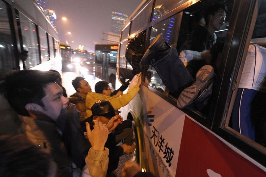 公交車站擁擠不堪,上車的乘客將車門堵死.部分乘客選擇爬窗入車.